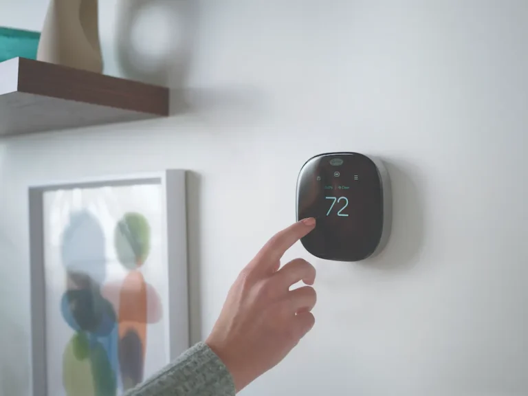 Hand reaching out to smart thermostat on wall